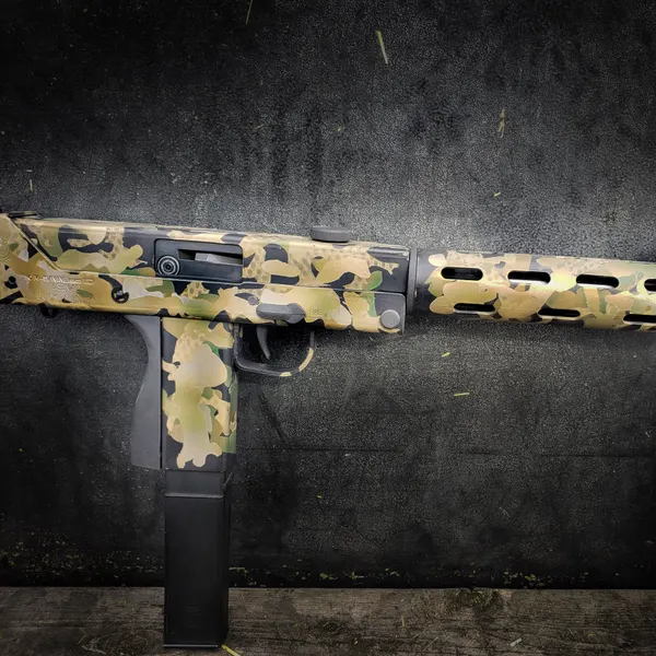 Side-folding 9mm carbine finished in multicam-pattern Cerakote against a dark background.