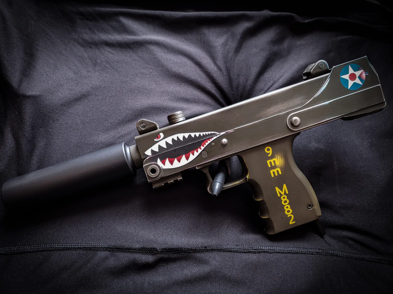 MAC-style 9mm pistol with a suppressor in olive drab Cerakote with a red and white shark-mouth graphic.